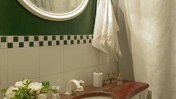 Un baño con un espejo redondo, paredes verdes, un lavabo blanco, una toalla blanca y una cortina de ducha.