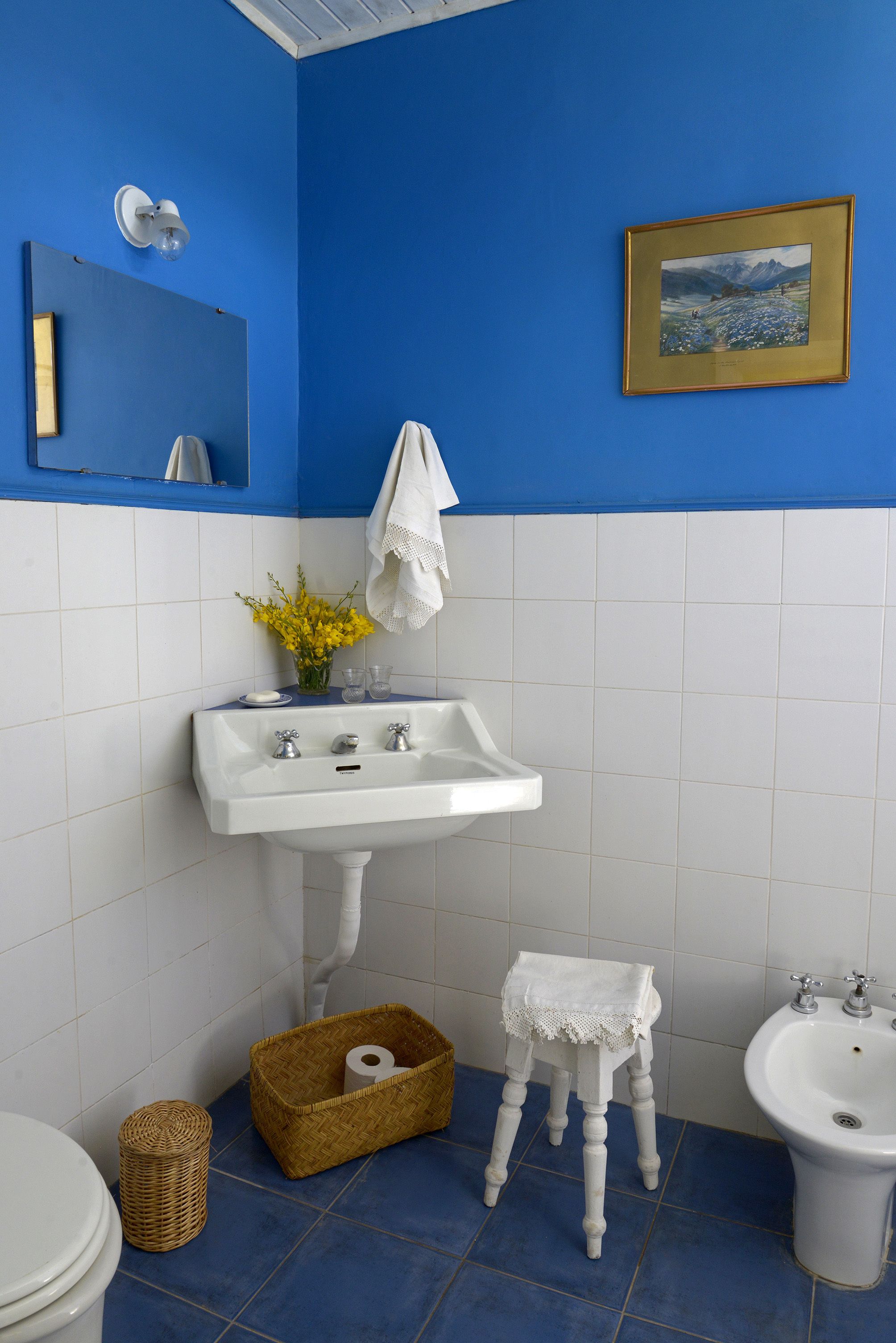 Un baño con un lavamanos blanco, un taburete de madera pequeño, una cesta de mimbre y un bidé.