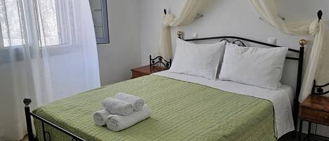 A neatly made bed with a green quilt, white pillows, and rolled white towels.