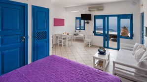 A room with a bed, a desk, chairs, a TV, and a view of the sea. - Folia Bianca Apartments (Santorini)