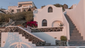 A white building with a stone facade, a staircase leading up to a second level, and a small window with a decorative grille. - Folia Bianca Apartments (Santorini)