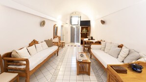 A spacious living room with a wooden sofa, a wooden coffee table, and a dining area with a table and chairs. - Folia Bianca Apartments (Santorini)