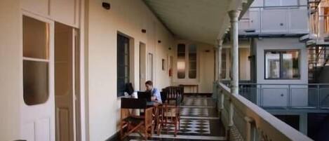 Un couloir avec un sol à carreaux, des meubles en bois et une personne assise à une table.