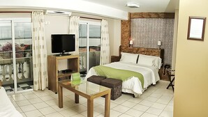 Una habitación de hotel con cama, televisión, mesa y balcón con cortinas.