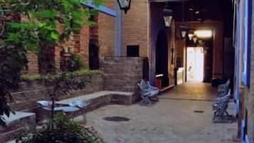 An outdoor courtyard with brick flooring, potted plants, and a pathway leading to a building entrance.