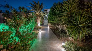 Un sendero en un jardín nocturno con palmeras y un edificio de piedra al fondo.
