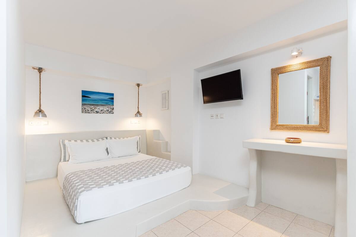 A bedroom with a bed, bedside lamps, a mounted TV, a mirror, and a painting on the wall.