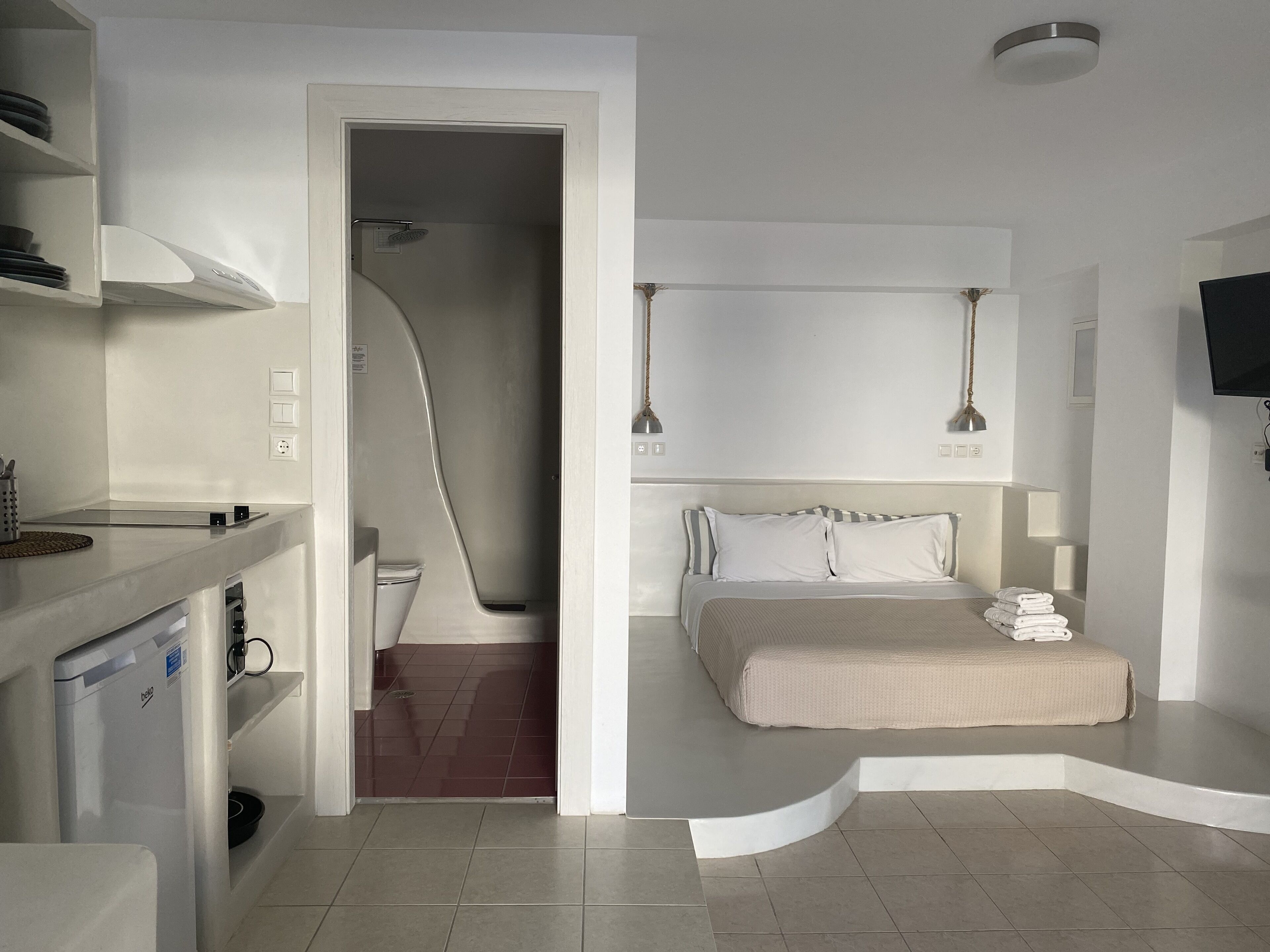 A modern hotel room with a bed, a desk, and a shower area.