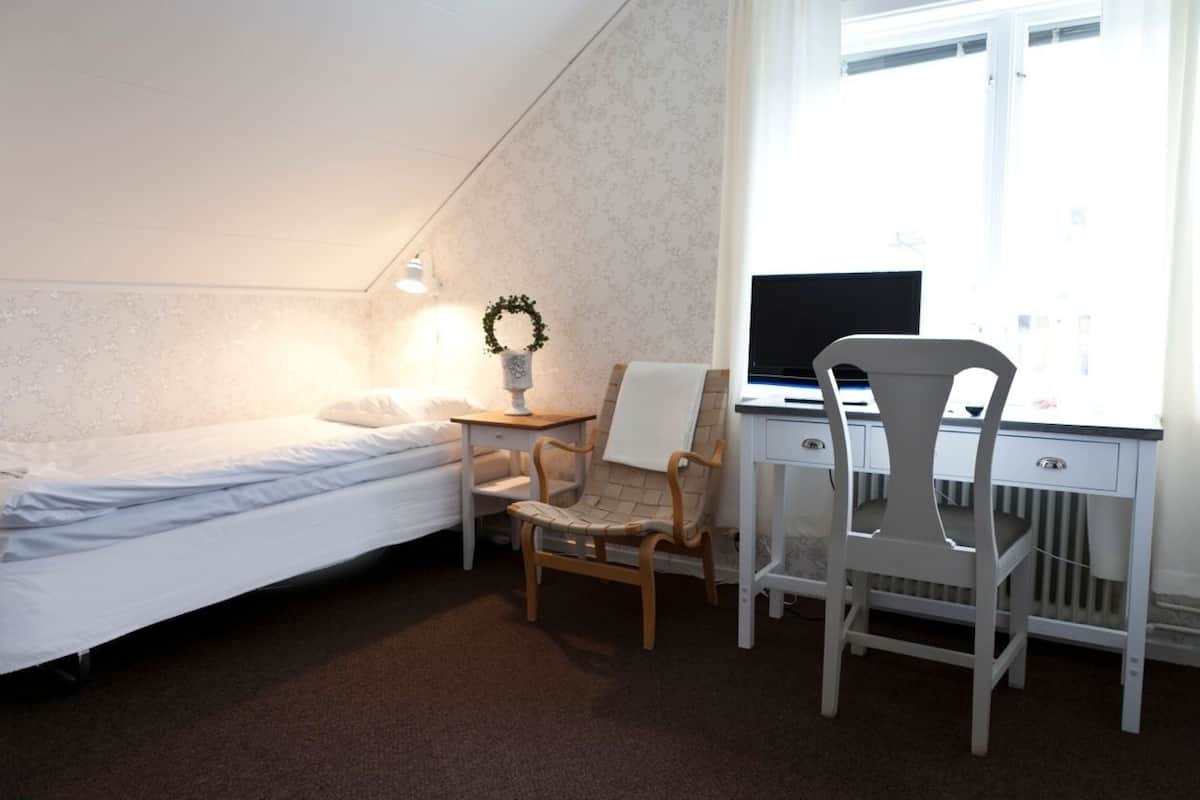 A bedroom with a bed, a desk, two chairs, a small table, and a window.