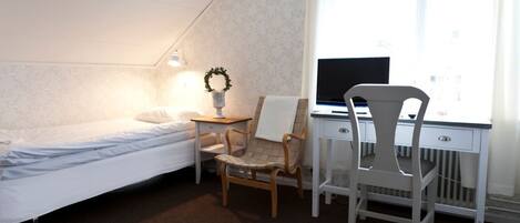 Ein Schlafzimmer mit Bett, Schreibtisch, zwei Stühlen, einem kleinen Tisch und einem Fenster.