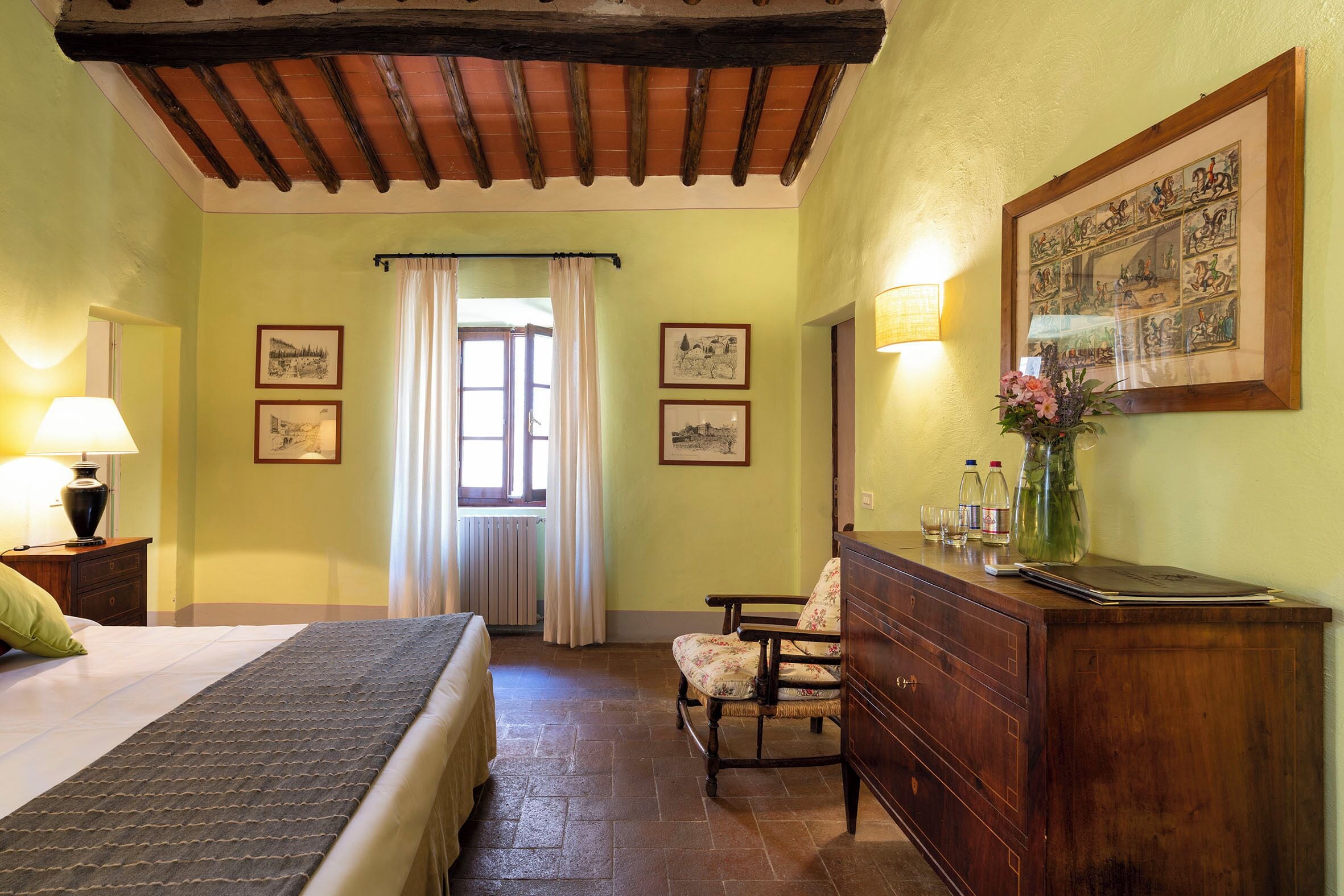 Une chambre à coucher avec un lit, une commode, une chaise et une fenêtre avec des rideaux.
