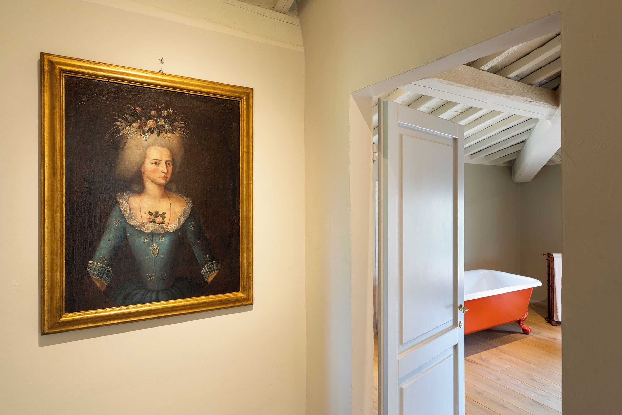 A room with a framed portrait on the wall, a white door, and a red bathtub in the corner.