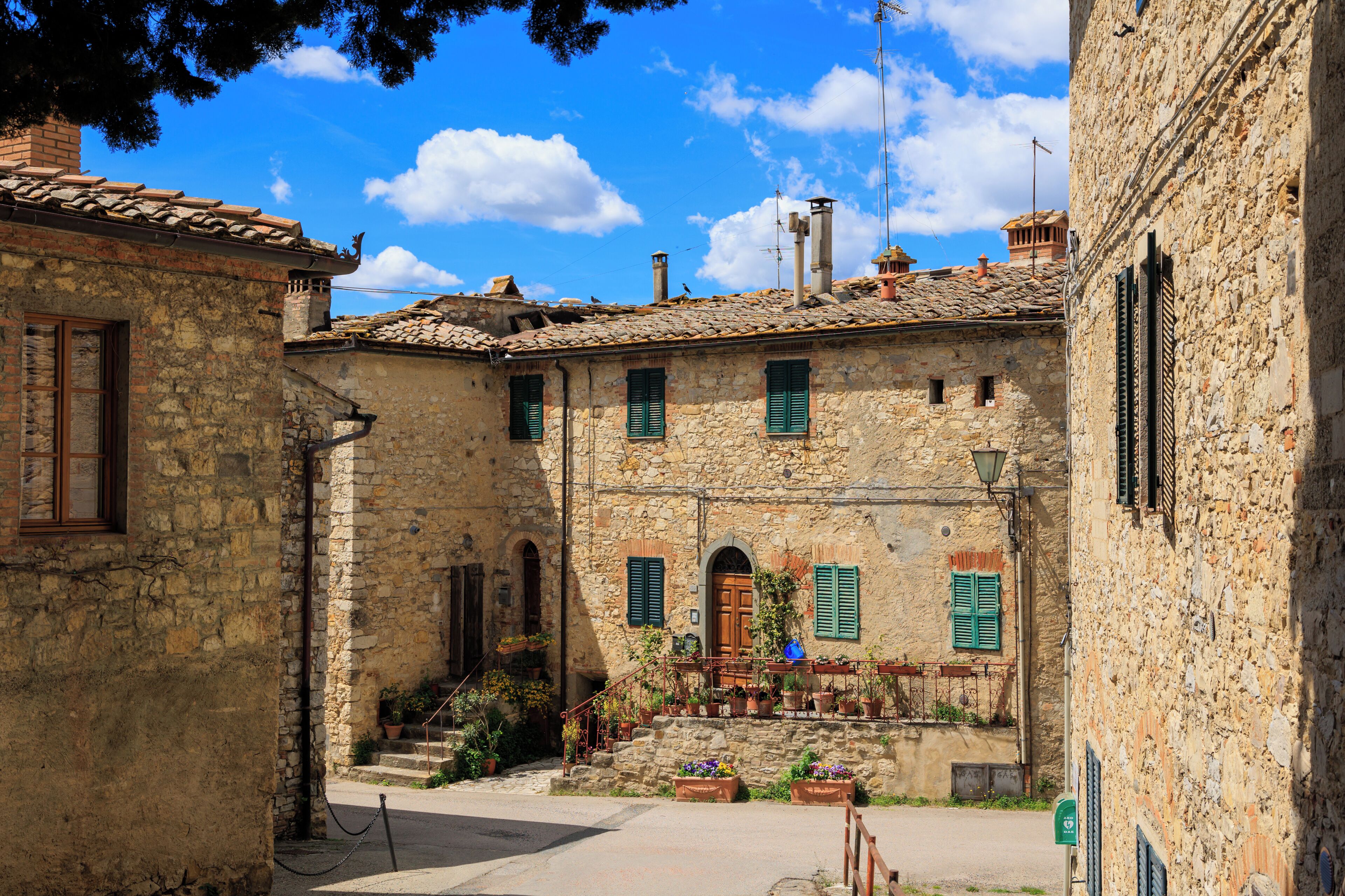 A stone building with a tiled roof, green shutters, and a small staircase leading to a door.