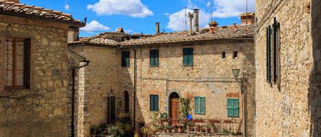 A stone building with a tiled roof, green shutters, and a small staircase leading to a door.