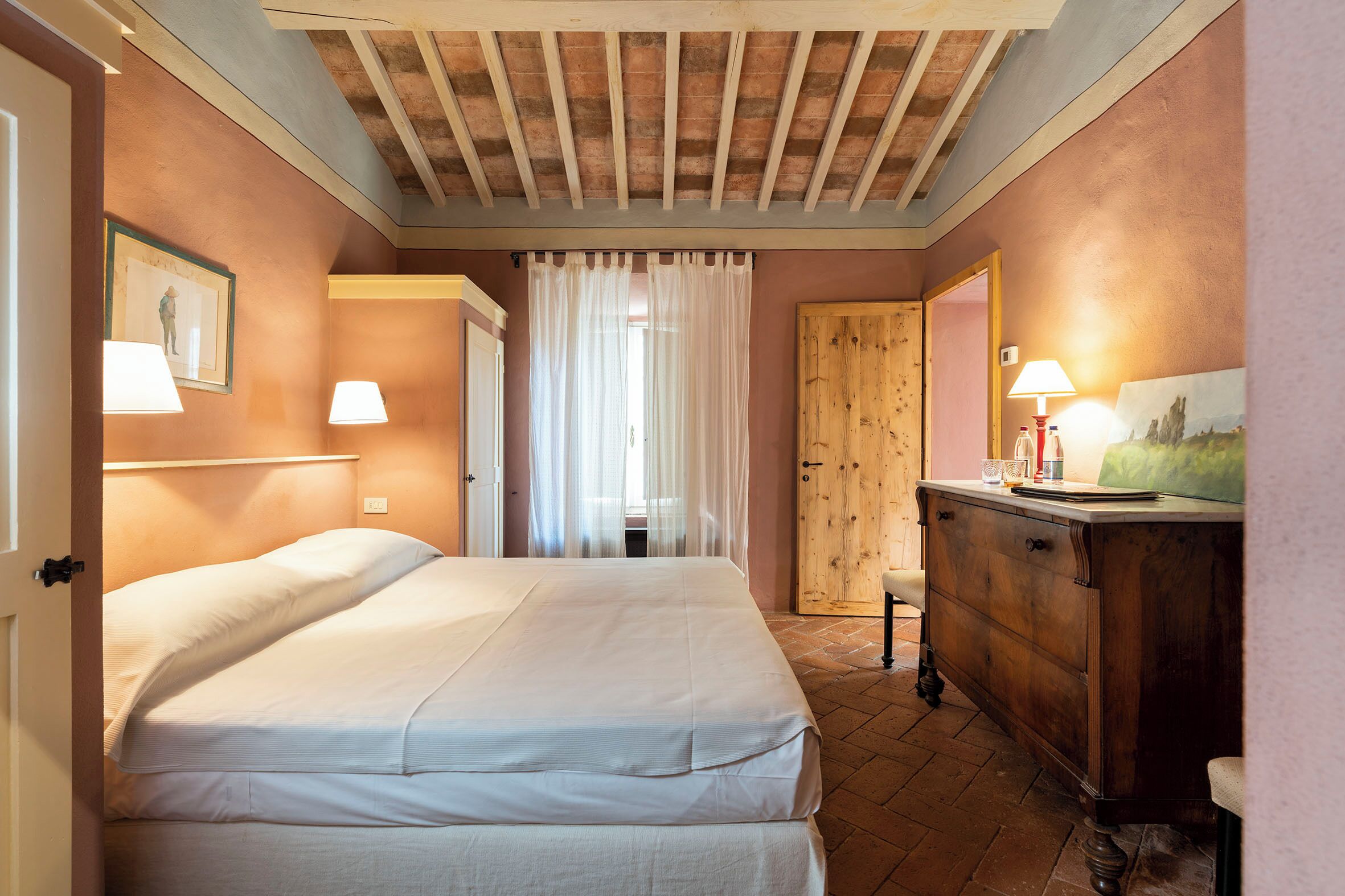 Un dormitorio con cama, cómoda de madera, puerta y ventana con cortinas.