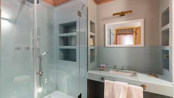 Een moderne badkamer met een douchecabine van glas, een witte wastafel en een spiegel boven het aanrecht.
