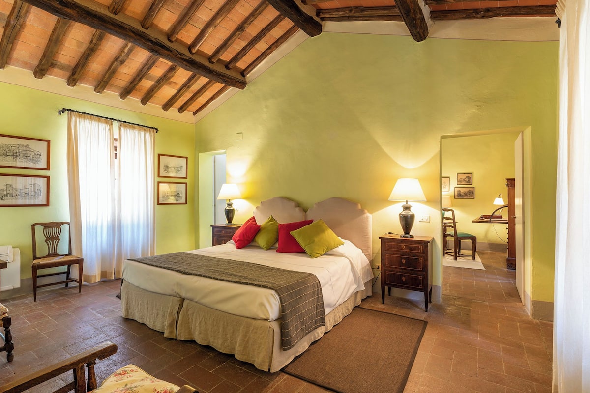 A bedroom with a large bed, two bedside tables with lamps, a chair, and a desk with a chair.