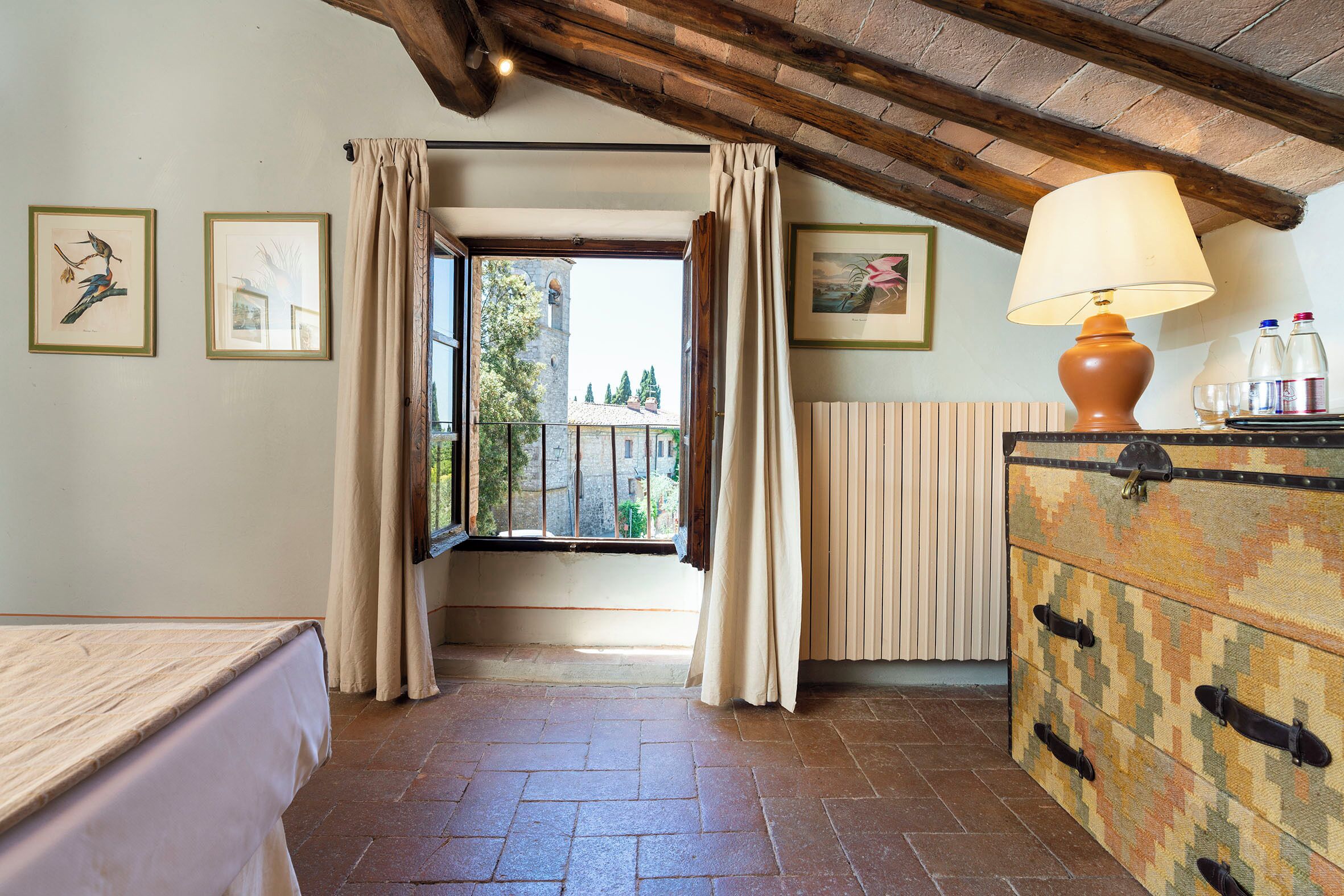 Una habitación con cama, cómoda, ventana con cortinas y lámpara.