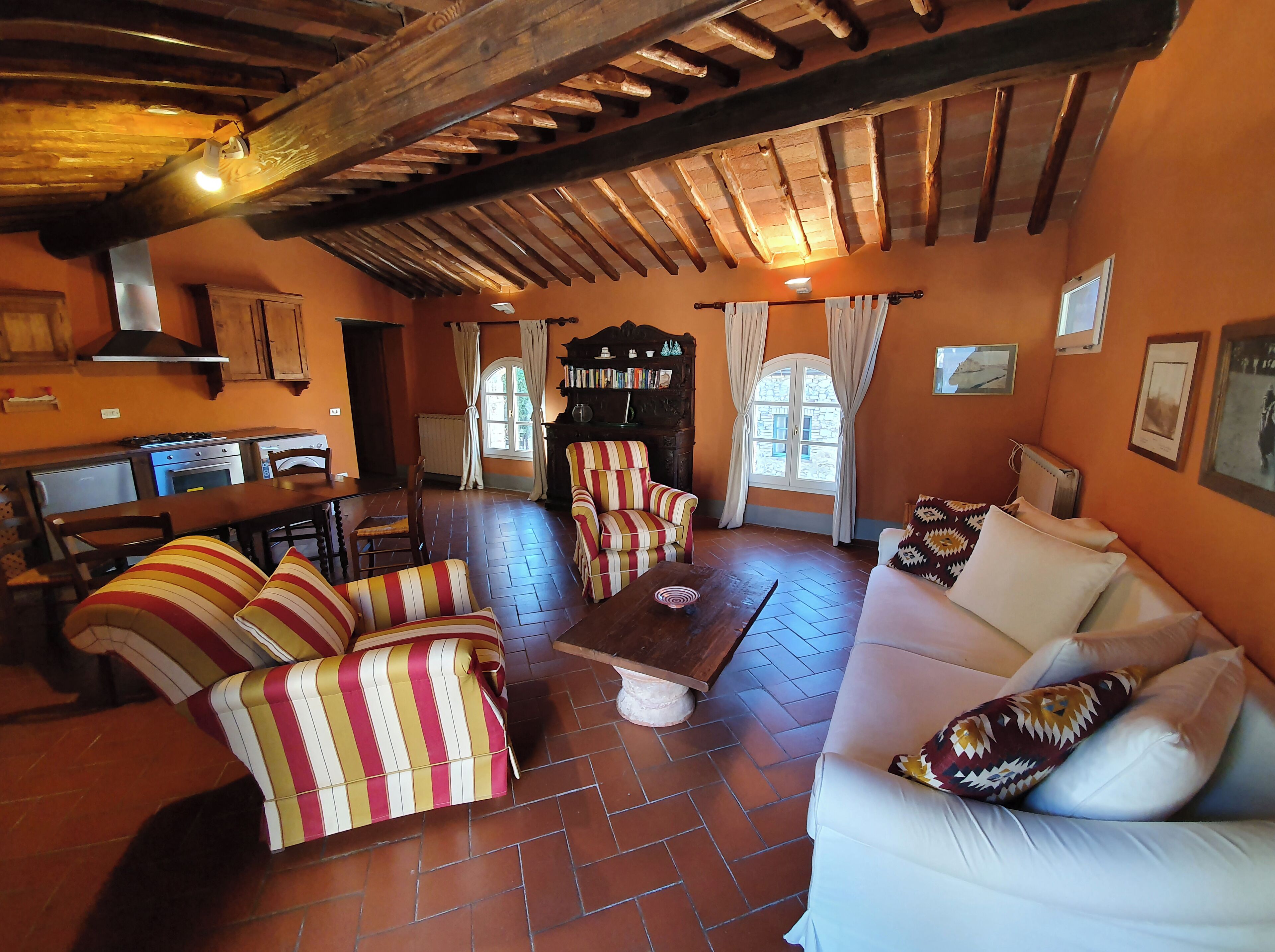 Una sala de estar acogedora con chimenea, sillones a rayas, un sofá y un comedor con una cocina al fondo.
