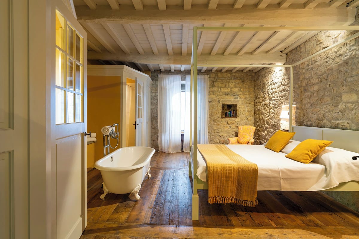 A bedroom with a wooden floor, a white bed, and a stone wall.
