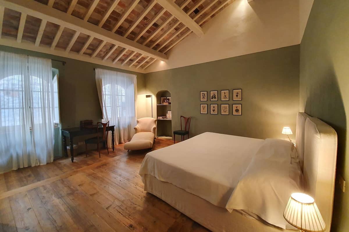 A bedroom with a wooden ceiling, a bed, a chair, a desk, and a lamp.