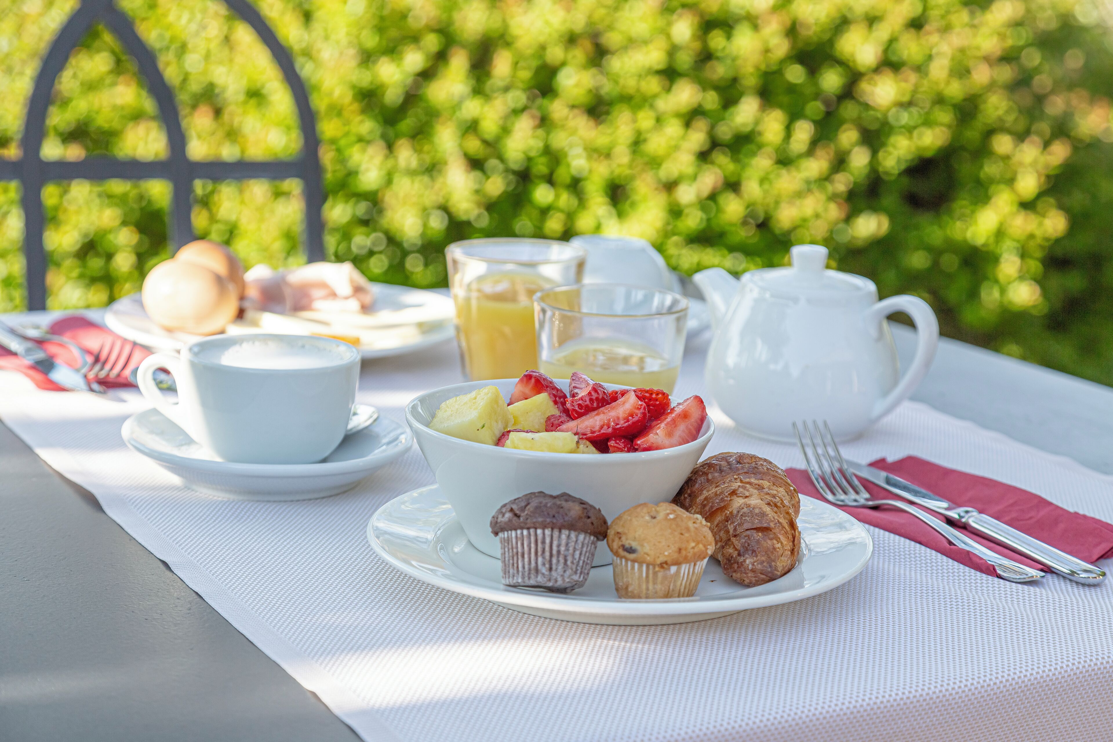 A table set with a white tablecloth, a bowl of fruit, muffins, a teapot, and cups.