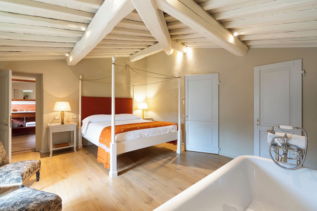 A bedroom with a four-poster bed, a white bathtub, and a wooden floor.