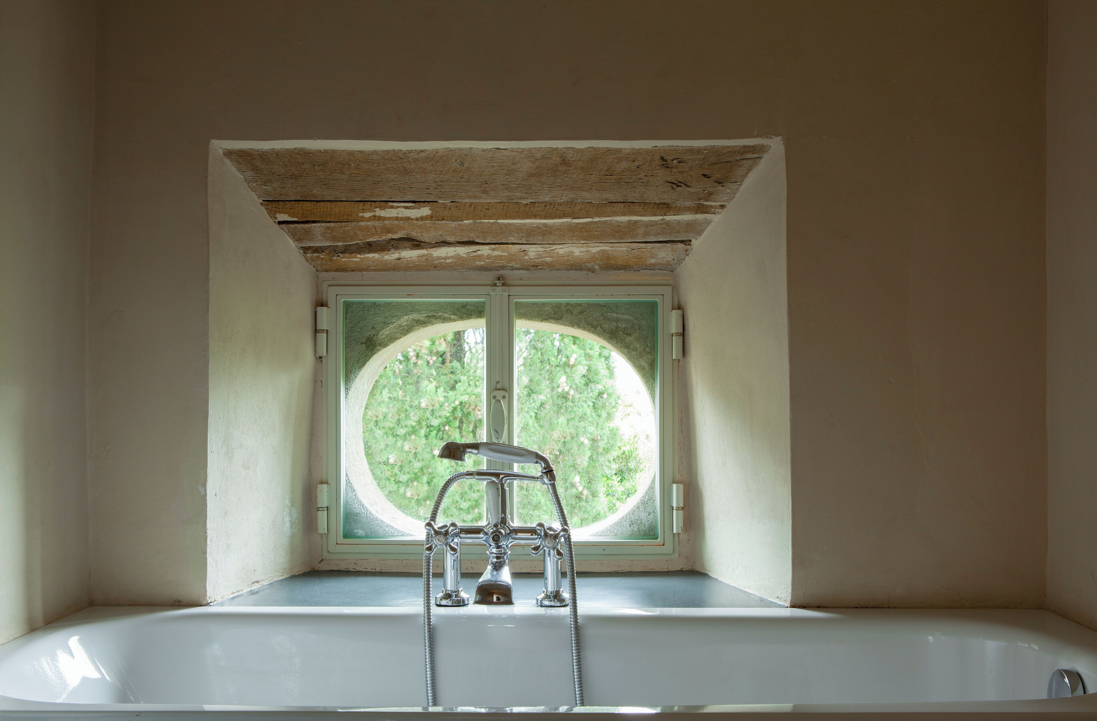 A bathroom with a bathtub, a window, and a wooden ceiling.