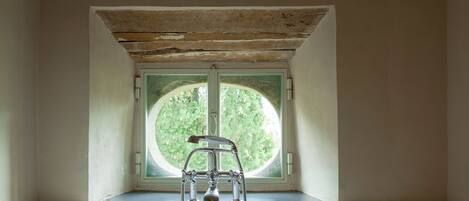 A bathroom with a bathtub, a window, and a wooden ceiling.