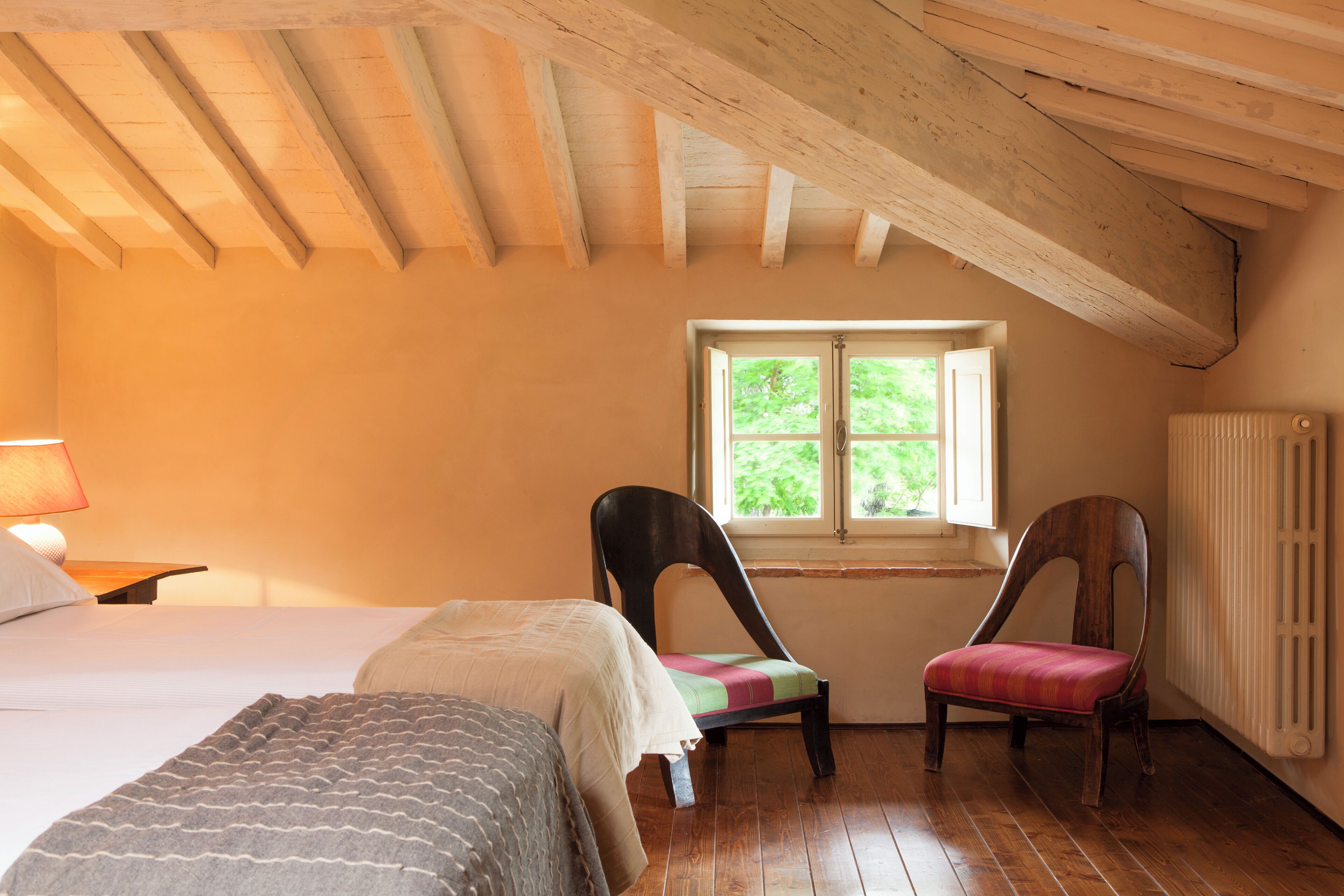 A bedroom with a bed, two chairs, a window, and a radiator.