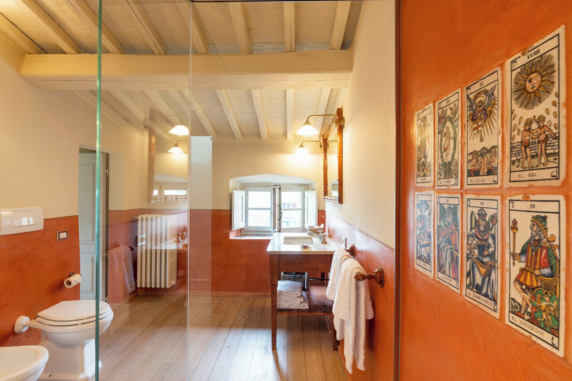 Une salle de bain avec un plancher en bois, des toilettes, un lavabo et un miroir. Il y a des cartes de tarot accrochées au mur.