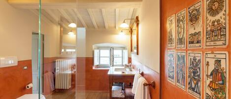 A bathroom with a wooden floor, a toilet, a sink, and a mirror. There are tarot cards on the wall.