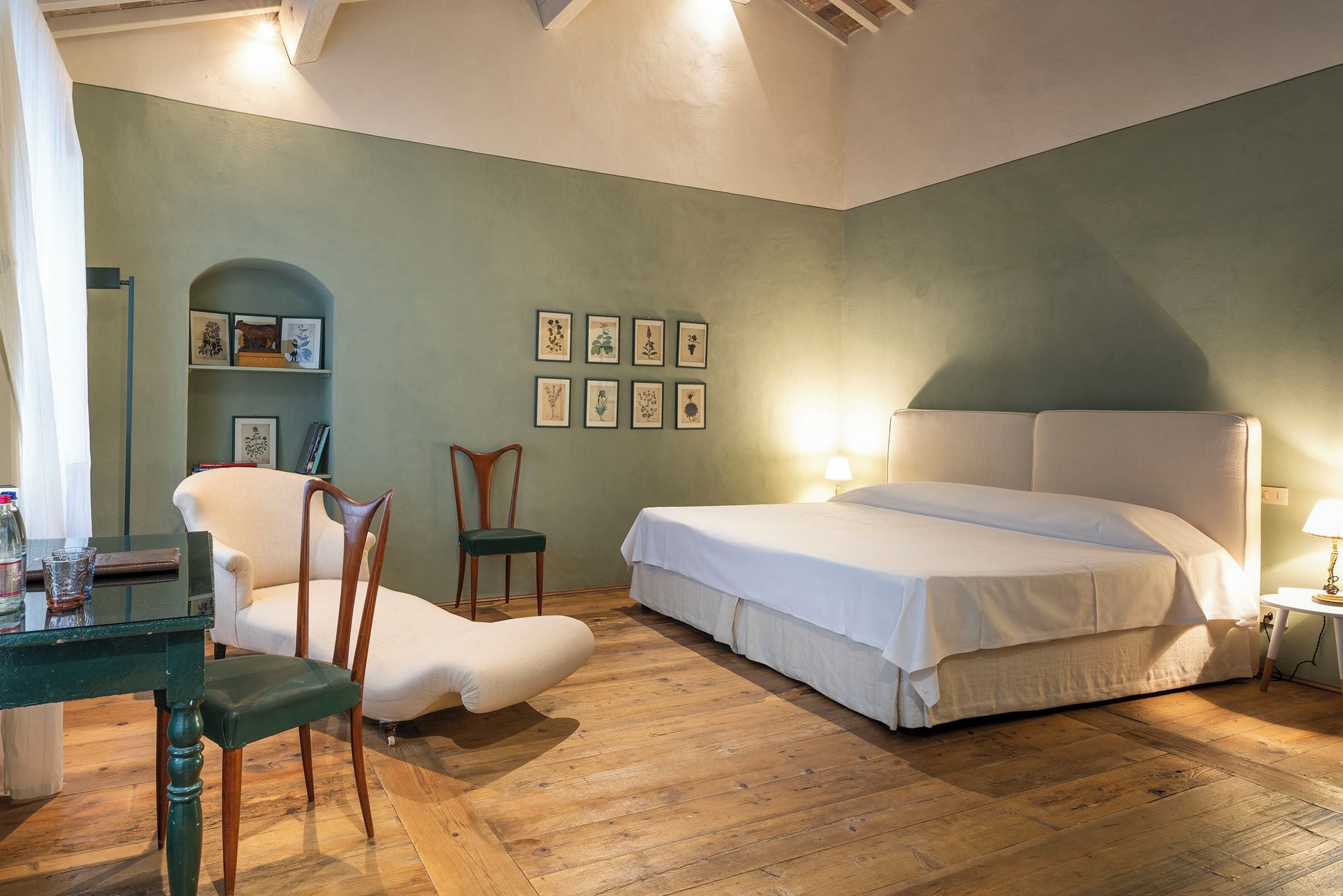 Una camera da letto con un letto, due sedie, un tavolino e quadri appesi al muro.