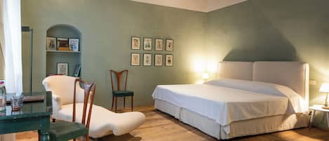A bedroom with a bed, two chairs, a small table, and framed pictures on the wall.