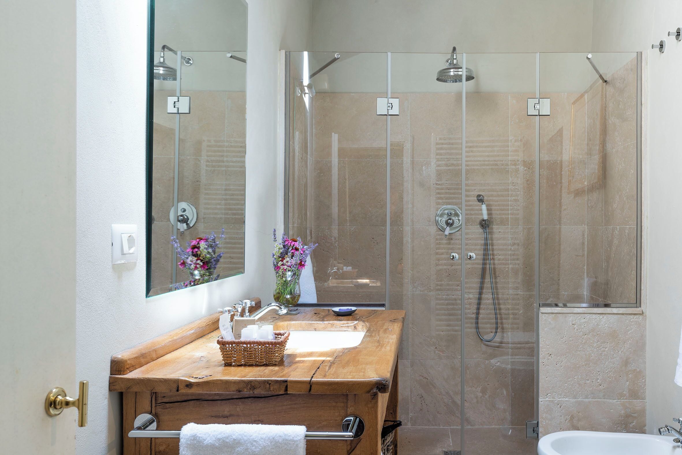 A bathroom with a wooden vanity, a glass shower enclosure, and a white sink.