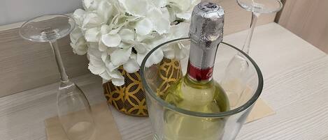 A table with a bottle of champagne, a glass, and a vase of white flowers.