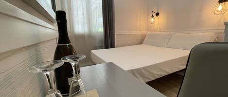 Habitación de hotel con cama, una mesa con botella y vasos, y una lámpara de pared.