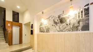 Un vestíbulo de hotel con una escalera, una puerta de madera y una lámpara fijada a la pared.