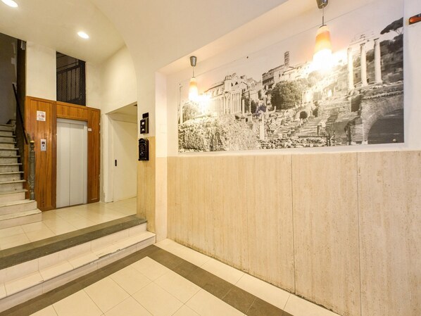 A hotel lobby with a staircase, a wooden door, and a wall-mounted light fixture. - Hotel Giotto Flavia (Rome)