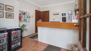Un área de recepción con un mostrador de madera, un refrigerador con bebidas, cuadros en la pared y un reloj.