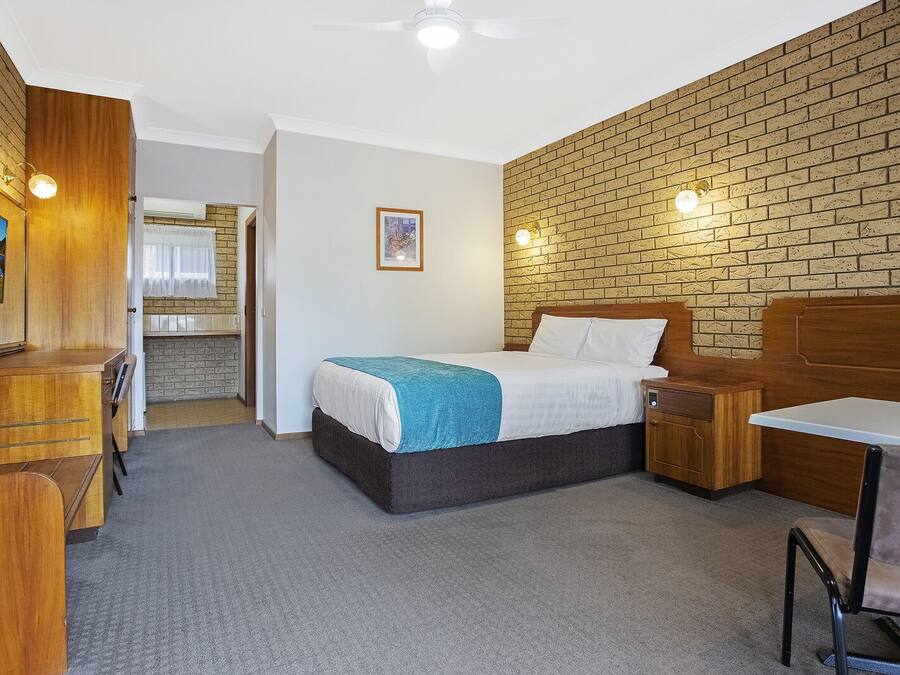 A hotel room with a bed, a desk, a chair, a TV, and a brick wall.