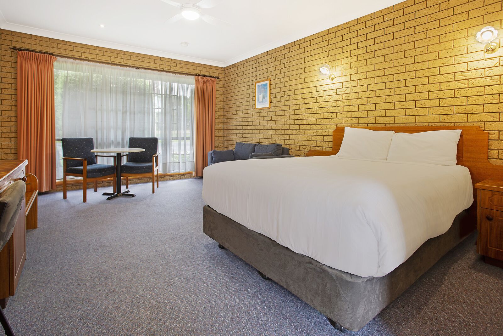 A hotel room with a large bed, a desk with a chair, a small table, and a window with curtains.