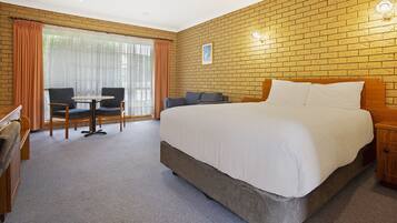 A hotel room with a large bed, a desk with a chair, a small table, and a window with curtains.