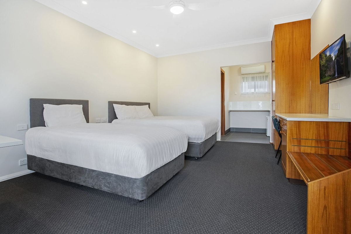 A hotel room with two beds, a wooden desk, a TV, and a bathroom visible through an open door.