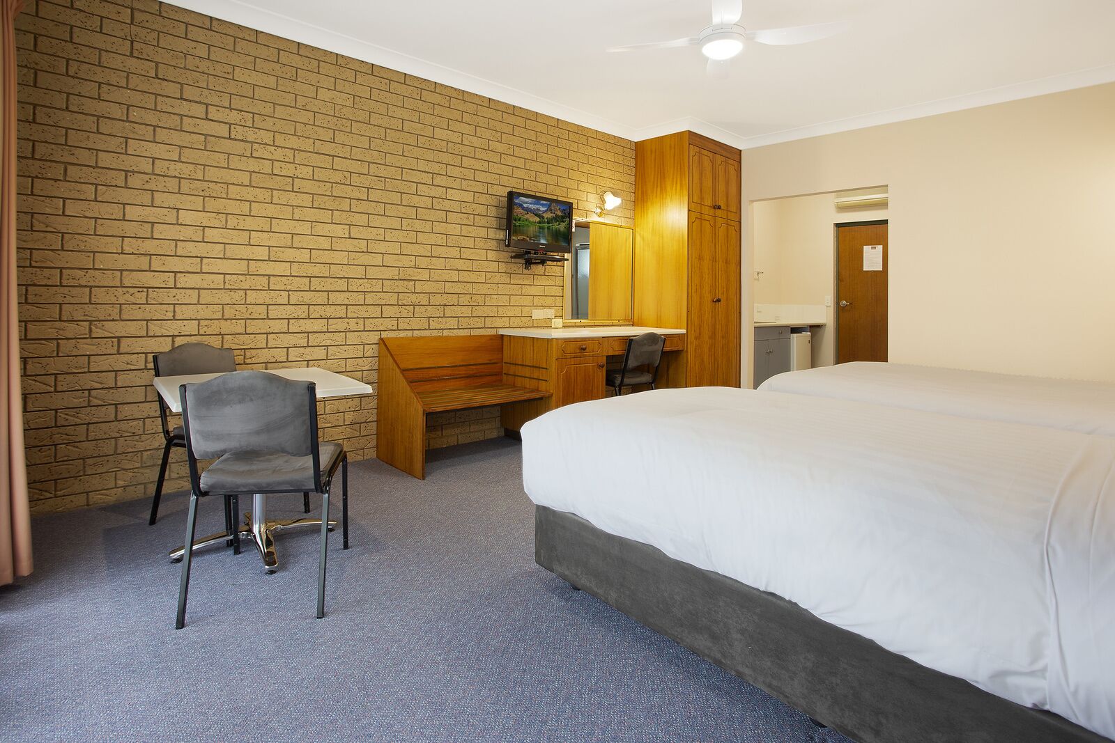 Une chambre d’hôtel avec un mur en briques, un lit, un bureau avec une chaise et un petit banc en bois.