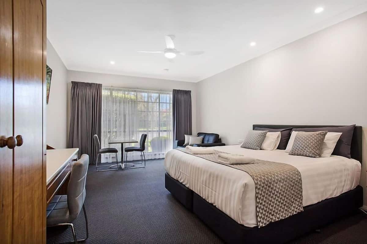 A hotel room with a bed, desk, chairs, and a window with curtains.