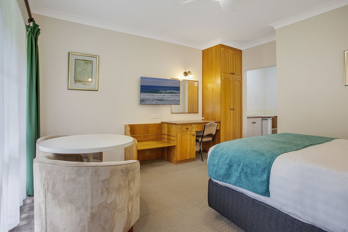 A hotel room with a bed, a desk, a chair, a round table, and a large window.