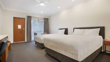 A hotel room with two beds, a desk, a chair, and a ceiling fan.