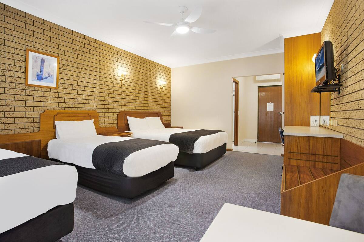 A hotel room with two beds, a desk, a television, and a door leading to a hallway.