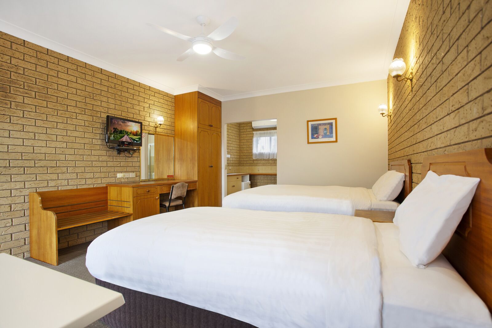 Une chambre d’hôtel avec deux lits, un bureau, une chaise, une télévision et un ventilateur de plafond.